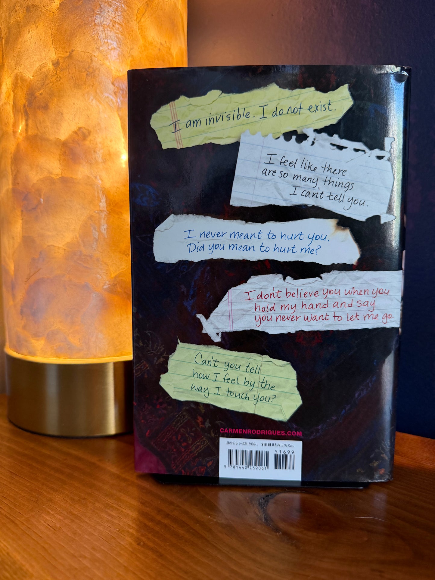 Book with torn paper sections on a wooden surface next to a lamp