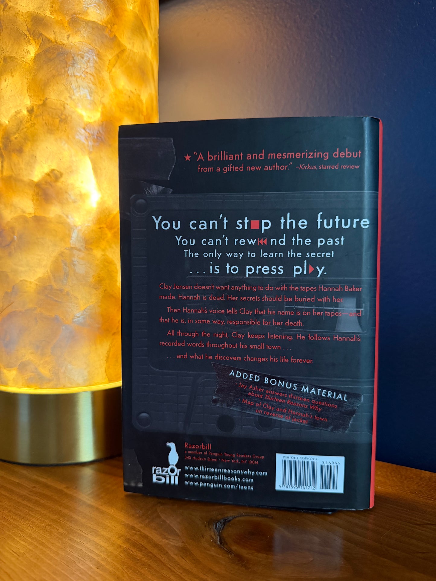 Book cover with text on a wooden surface and lamp in the background
