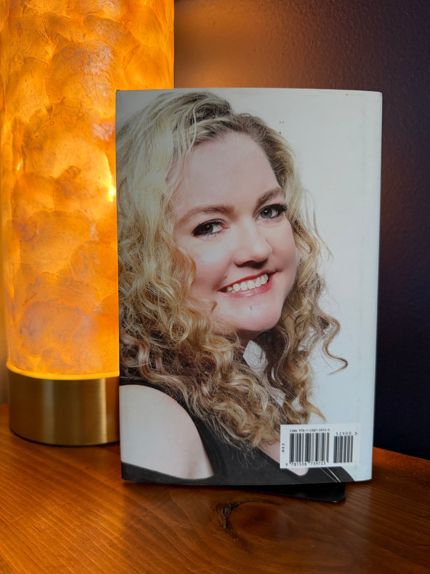 Book with a woman's face on the cover next to a lamp on a wooden surface