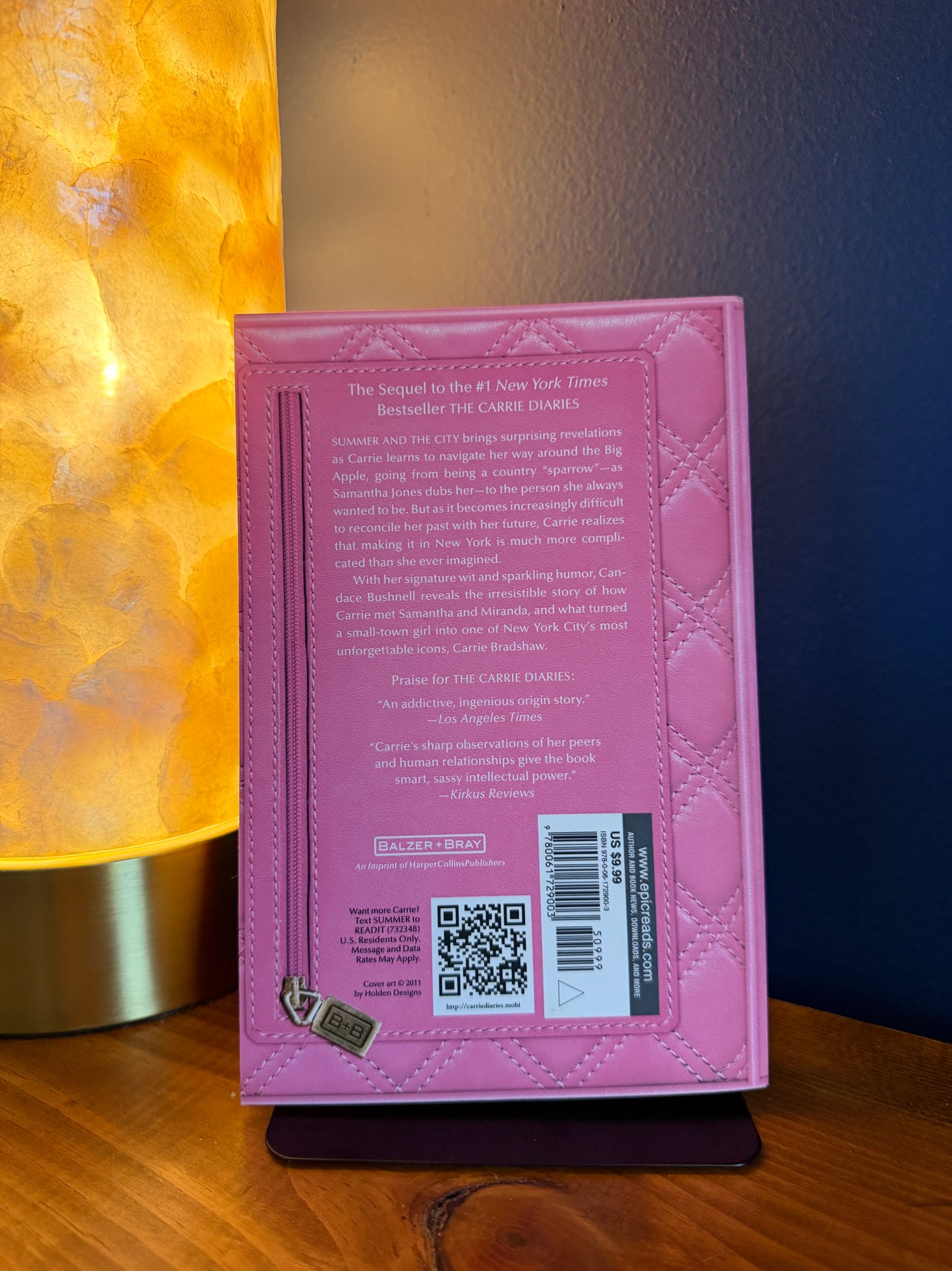 Pink book with text and a QR code on a wooden surface with a warm light source.