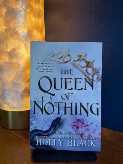 Book titled 'The Queen of Nothing' by Holly Black on a stand with a warm light source.