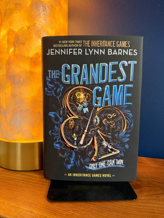 Book titled 'The Grandest Game' by Jennifer Lynn Barnes on a wooden surface with a blue background.
