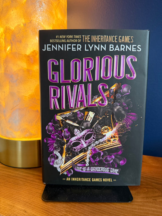 Book titled 'Glorious Rivals' by Jennifer Lynn Barnes on a stand with a lamp in the background.