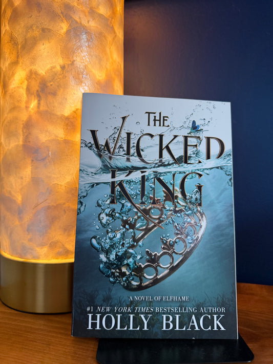 Book titled 'The Wicked King' by Holly Black on a wooden surface with a blurred background