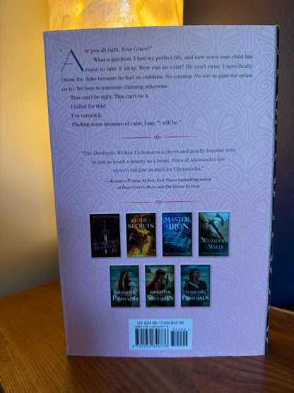 The back cover of a hardcover book lying on a wooden surface, showing the title 'The Darkness Within Us' and several small book cover thumbnails.